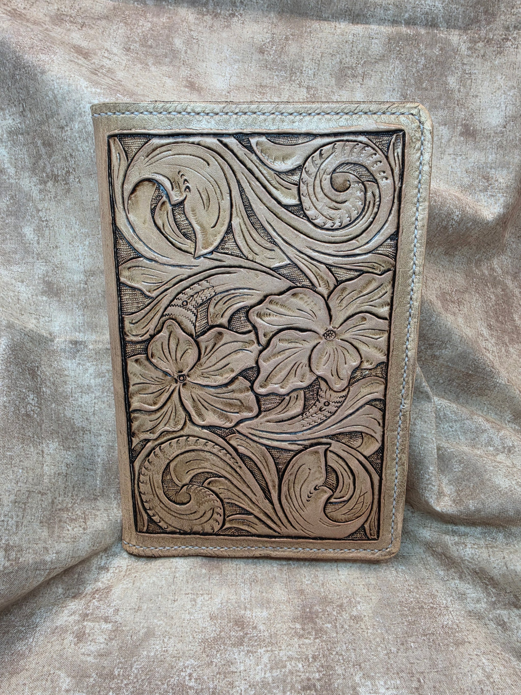 A rectangular tooled leather folio cover with intricate floral and scroll embossed designs.